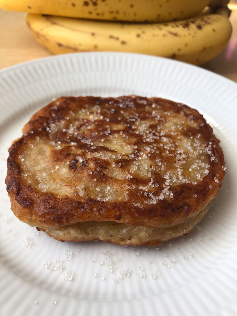 Jamaican banana fritters served on a plate, overripe bananas in the background