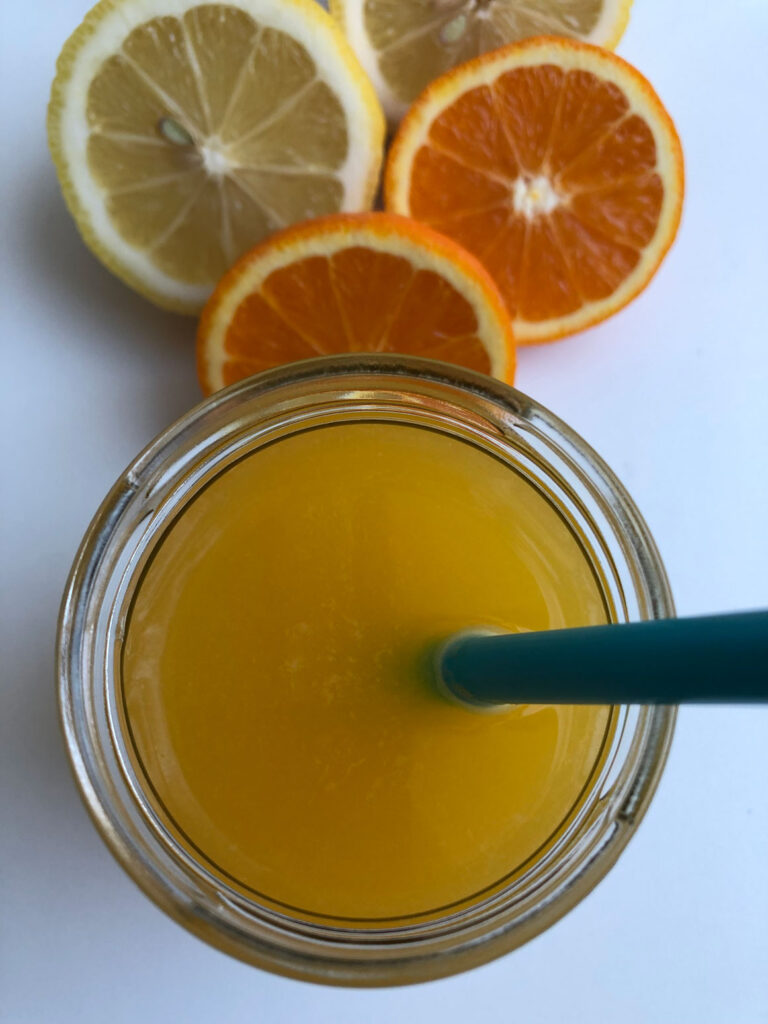 Homemade orange lemonade in a glass with a straw, orange and lemon halves in the background, bird's eye view