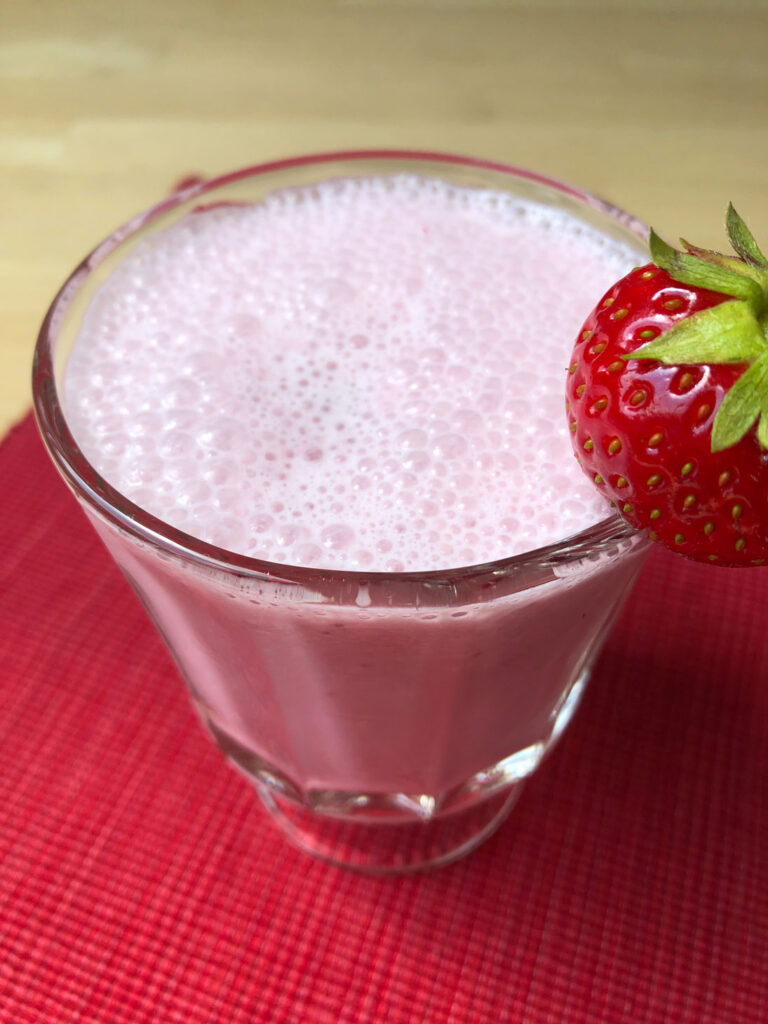 Strawberry milk in a glass with a whole strawberry on the rim