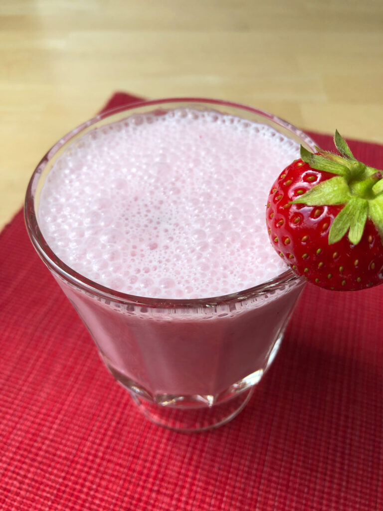 Strawberry milk in a glass with a whole strawberry on the rim