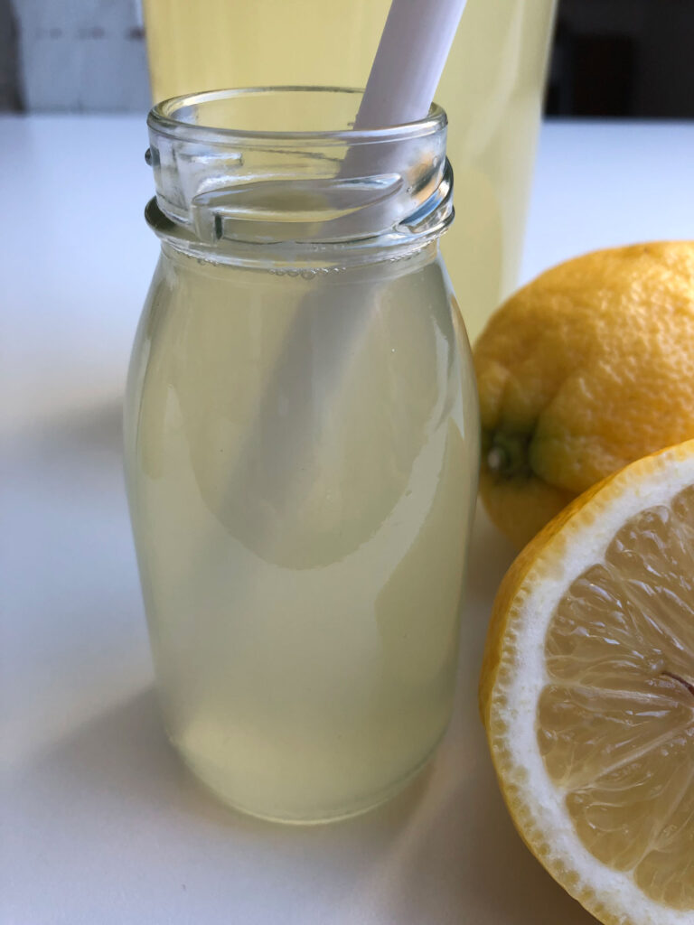 Healthy homemade lemonade in a glass with a straw, lemons beside the glass.