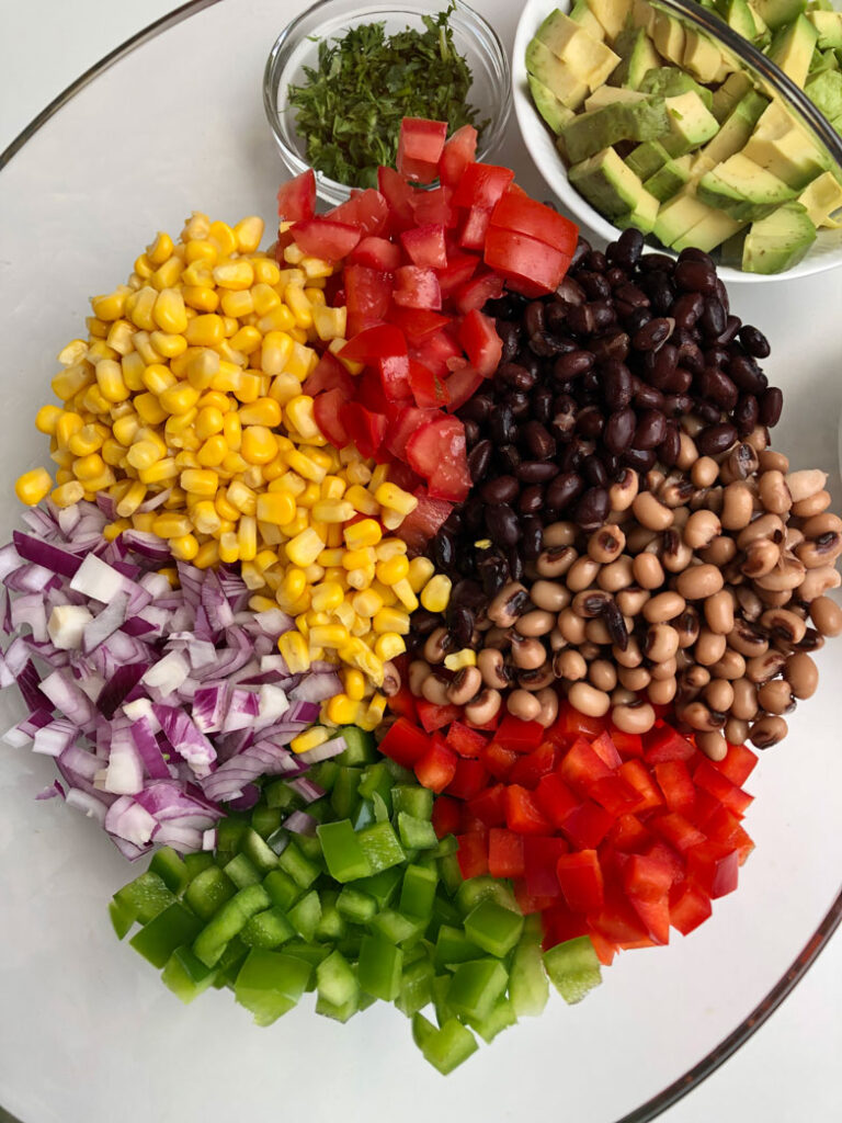 Cowboy caviar ingredients gathered in a large serving bowl. Diced avocado and chopped cilantro in two separate prep bowls next to it.