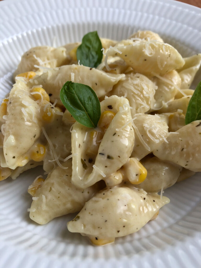 Creamy corn pasta on a plate garnished with a few basil leaves.