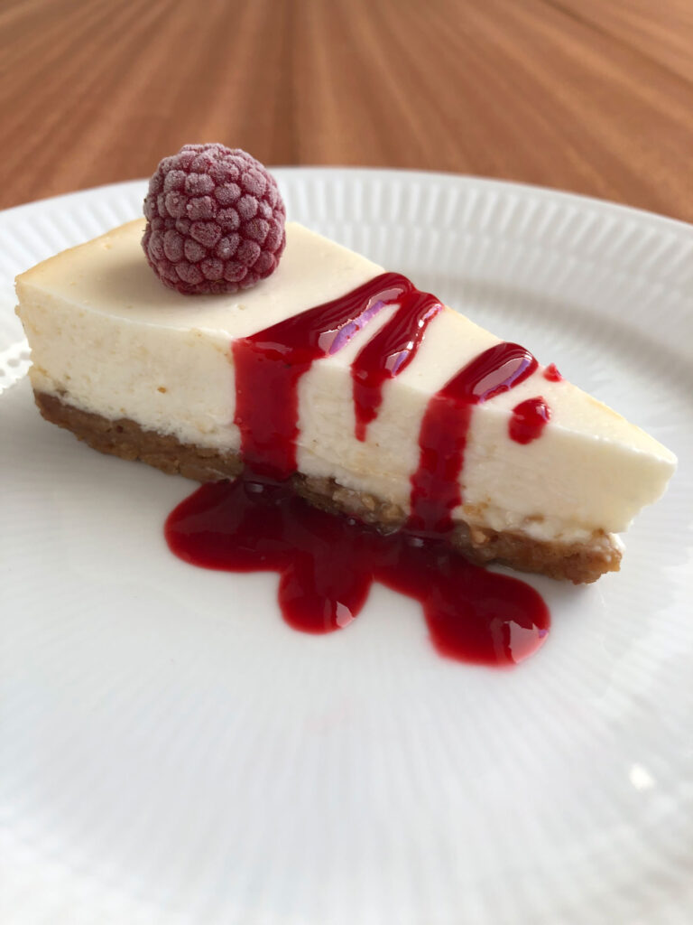 Healthy Greek yogurt cheesecake, topped with a frozen raspberry and raspberry sauce, on a plate.