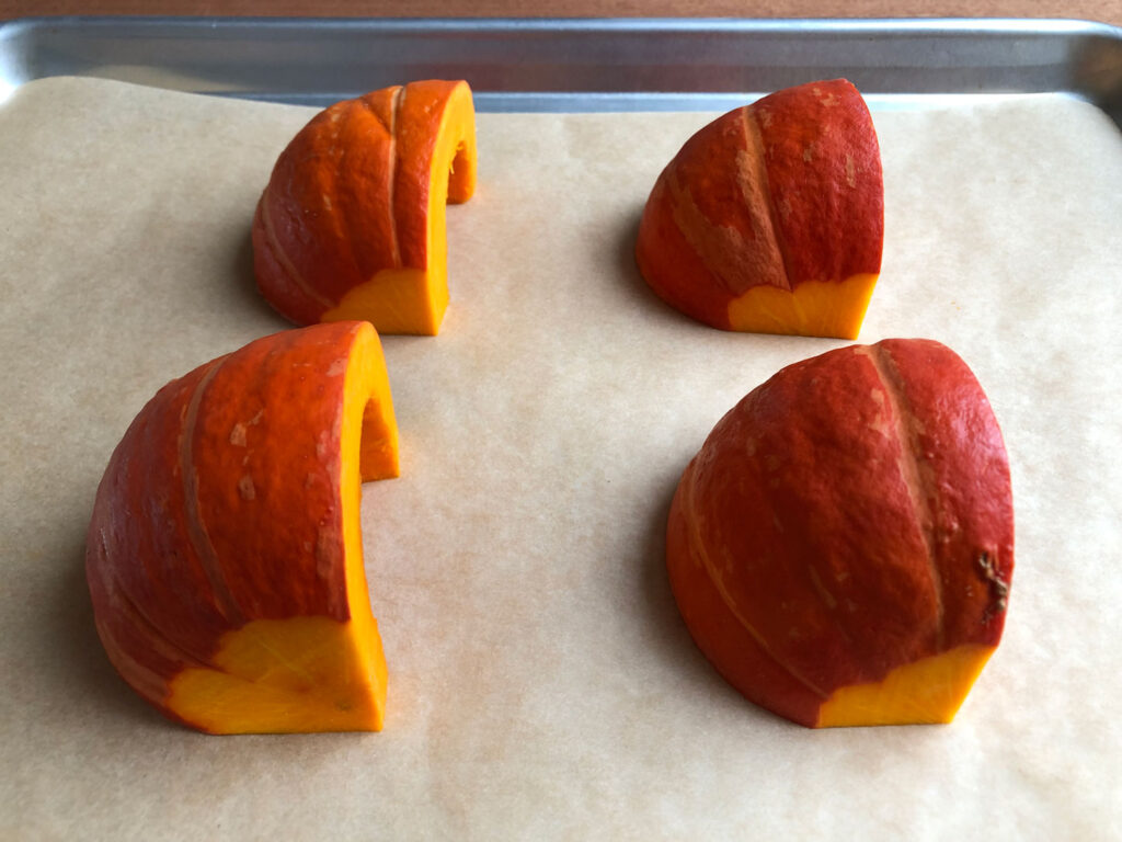 Four quarters of pumpkin placed on a baking sheet.