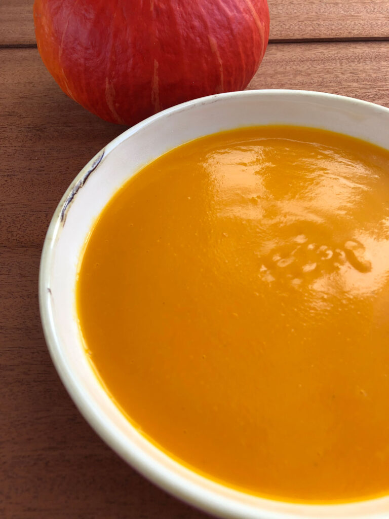 Easy pumpkin soup served in a bowl, a pumpkin in the background.