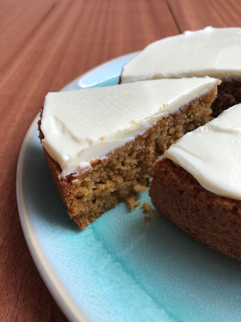 A slice cut out of a carrot cake with cream cheese frosting on a cake plate.