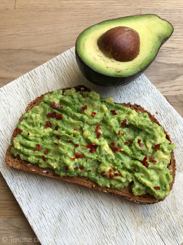 Avocado toast served on a wooden board with an avocado half in the background.