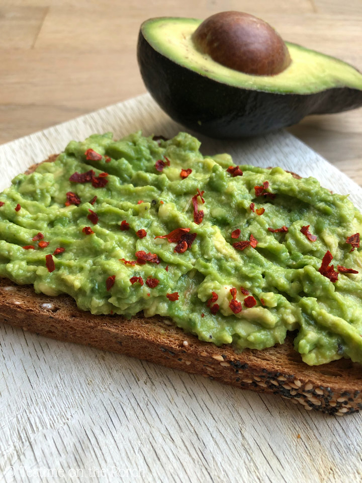 Avocado toast served on a wooden board with an avocado half in the background.