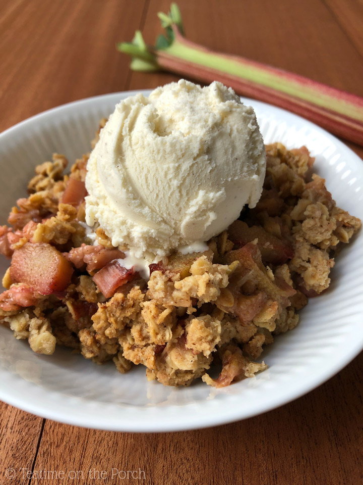 Healthy Rhubarb Crisp Recipe Rhubarb crisp served with a scoop of vanilla ice cream on top in a bowl with a rhubarb stalk in the background.