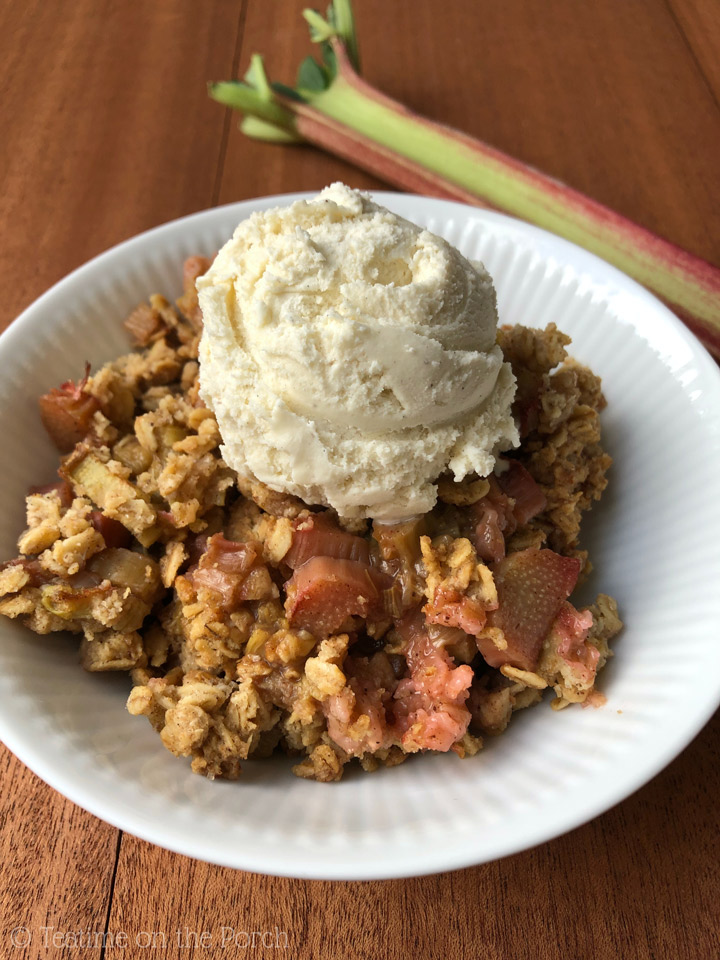 Healthy Rhubarb Crisp Rhubarb crisp served with a scoop of vanilla ice cream on top in a bowl with a rhubarb stalk in the background.