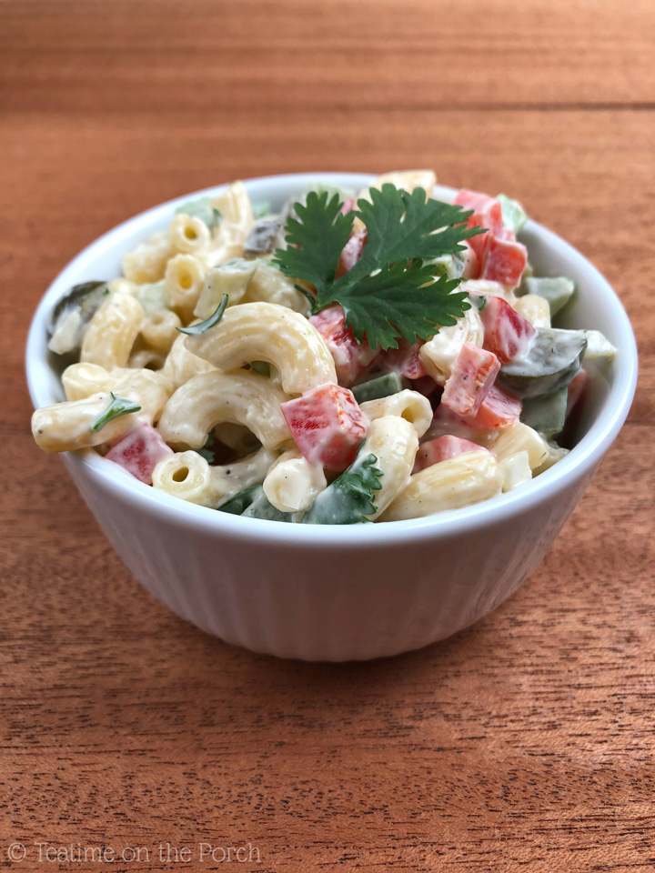 Macaroni Salad Recipe Colorful classic macaroni salad in a small bowl, decorated with a flat-leaf parsley leaf.