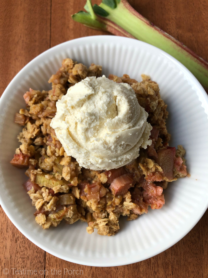 The Best Healthy Rhubarb Crisp Rhubarb crisp served with a scoop of vanilla ice cream on top in a bowl with a rhubarb stalk in the background.