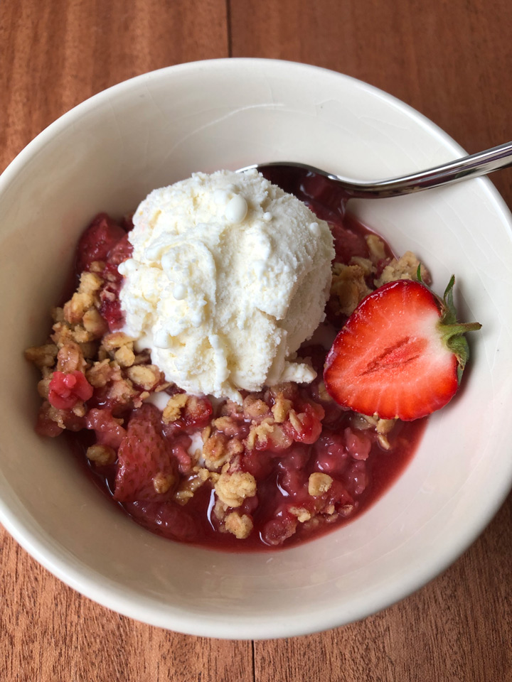 Healthy Strawberry Crisp Healthy strawberry crisp, served in a bowl with a scoop of vanilla ice cream on top and decorated with half a strawberry.