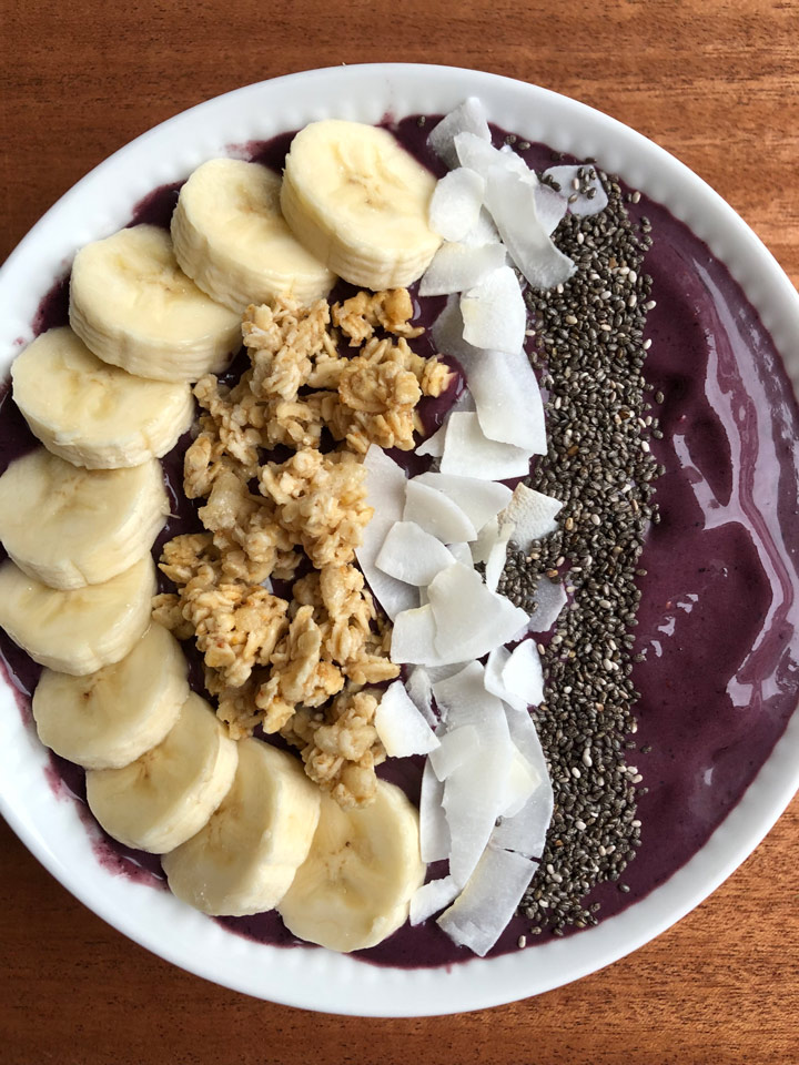 Acai bowl topped with banana, granola, coconut flakes, and chia seeds.