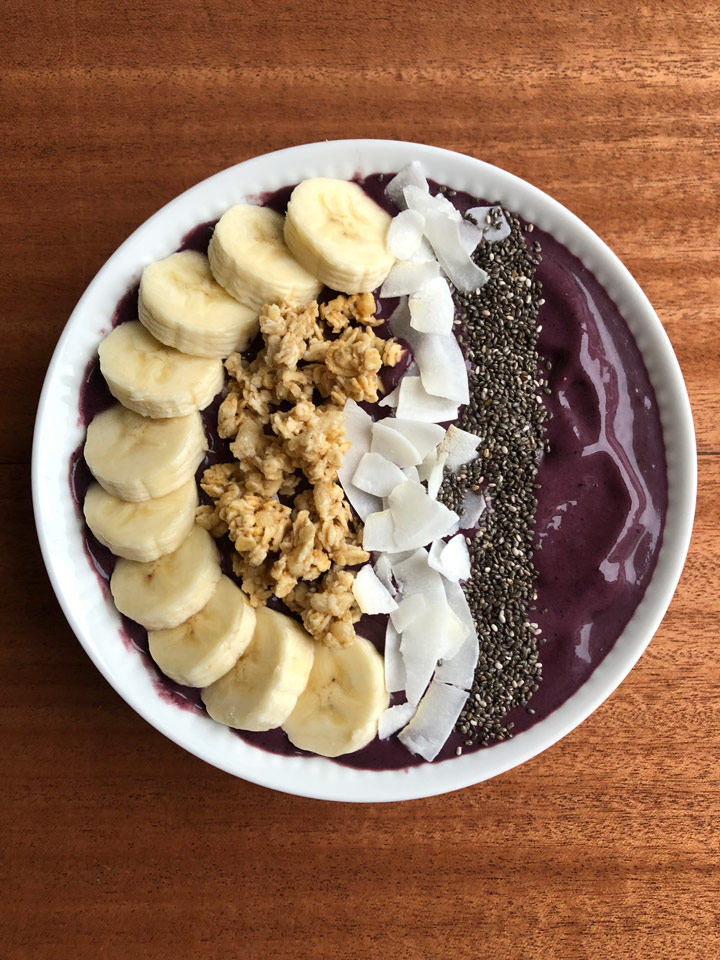 Acai bowl topped with banana, granola, coconut flakes, and chia seeds.